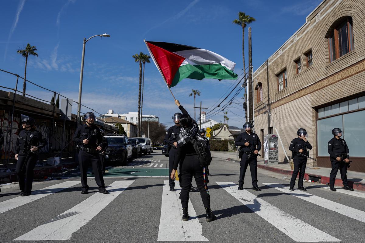 A protester waves a Palestinian flag in front of law enforcement officers as hundreds demonstrate in support of Palestinians calling for a ceasefire in Gaza near the Dolby Theatre.