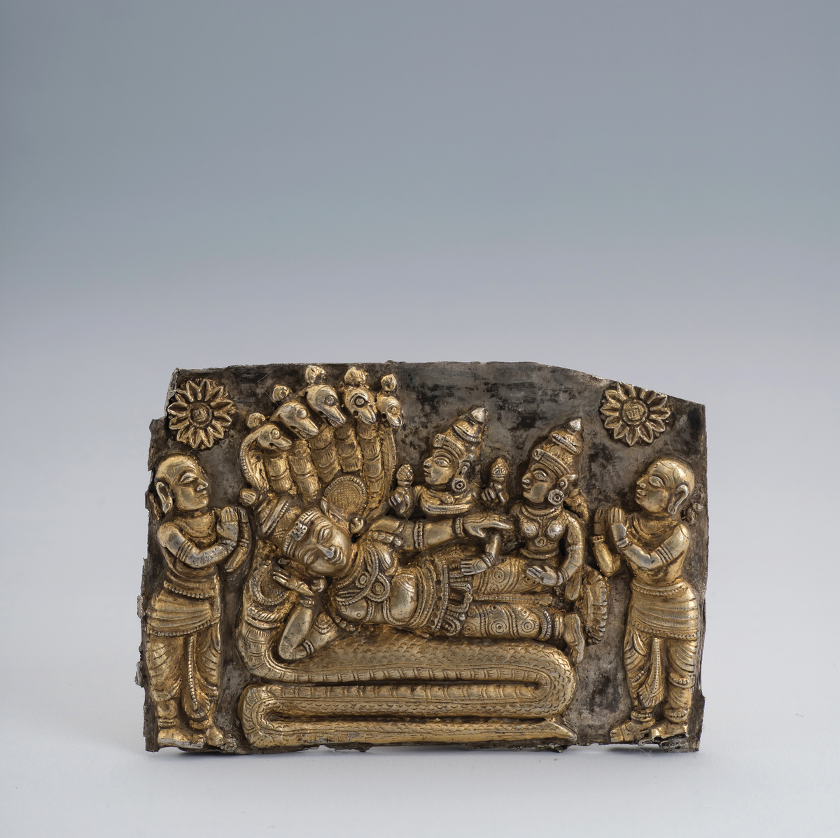 Een zilveren plaquette met een afbeelding van Vishnu op de slang Shesha, geflankeerd door Lakshmi.