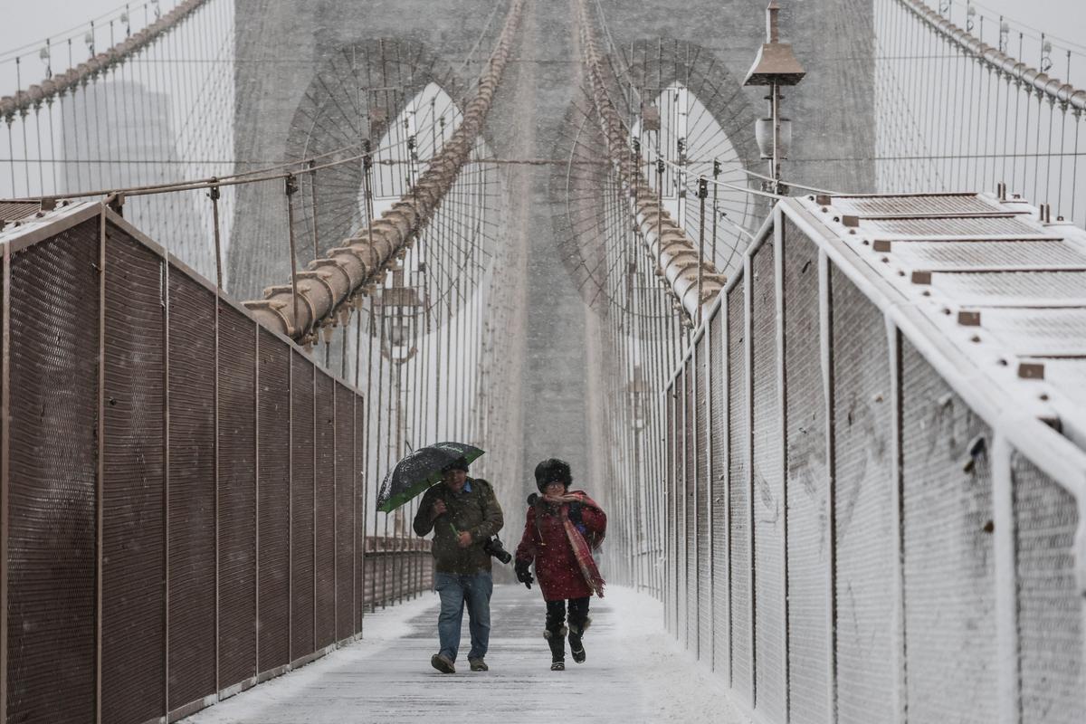 People walk across the Brooklyn Bridge as snow falls during a winter storm in New York City, U.S., on February 22, 2026. 