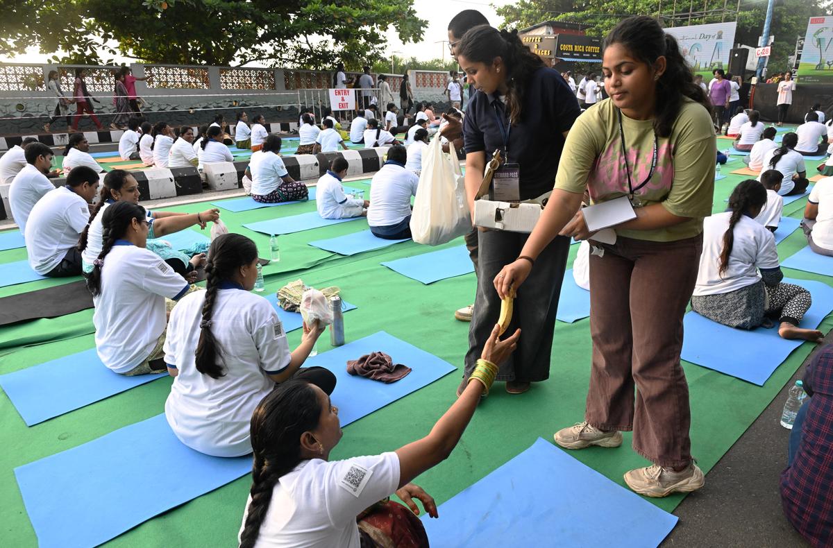 Volunteers distributing snacks and fruits during the International Yoga Day celebrations on the Beach Road in Visakhapatnam on Saturday (June 21, 2025).