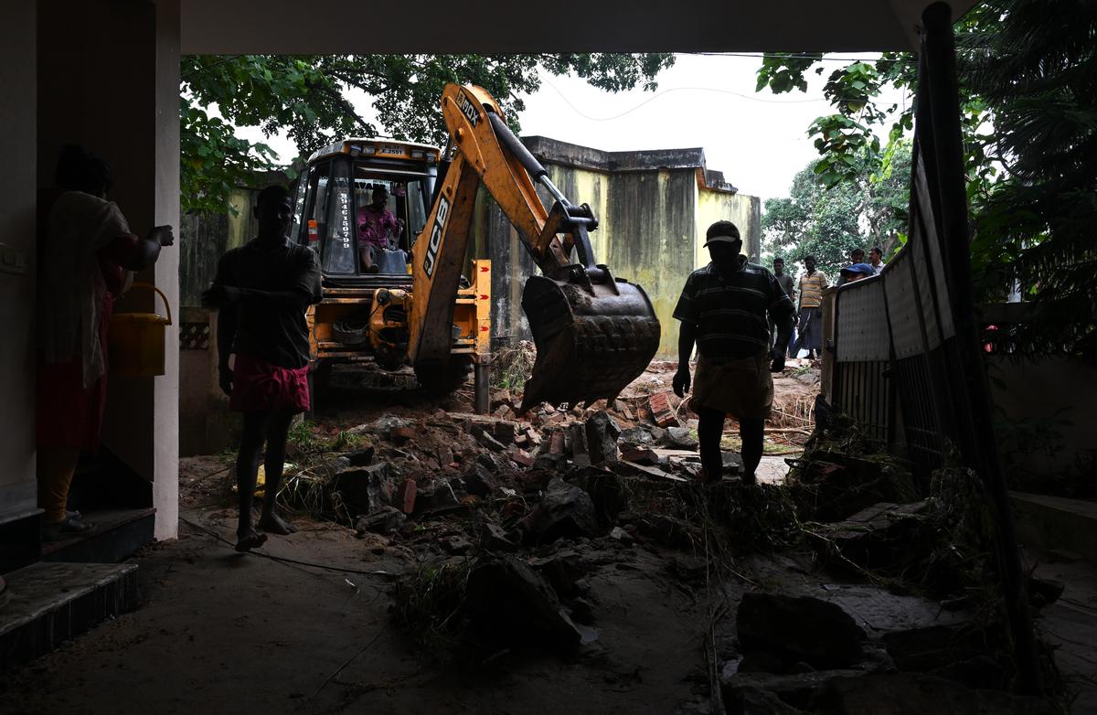 An excavator clears debris from a damaged house.