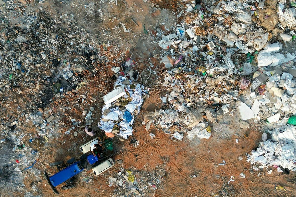 An aerial view shows a worker operating a tractor at a landfill next to a lake in Bengaluru on April 15, 2026. (Photo by Idrees MOHAMMED / AFP)