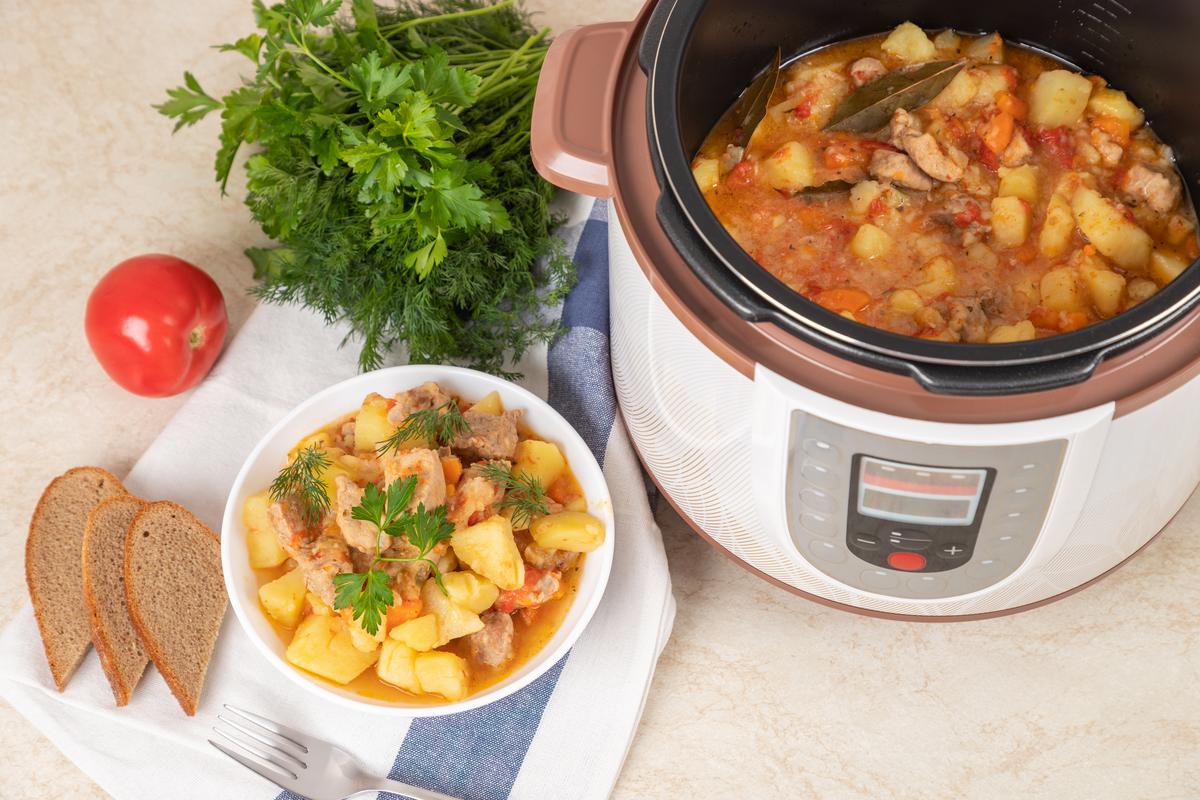 Meat stewed with potatoes, carrots, tomatoes and spices in modern multi cooker on kitchen table. Meat stewed with potatoes, carrots, tomatoes and spices in modern multi cooker on kitchen table.