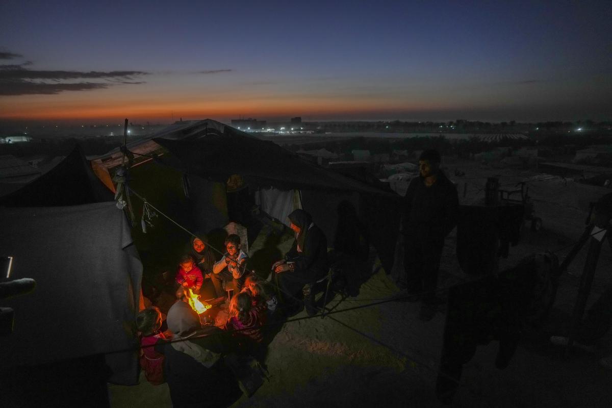 Reda Abu Zarada, 50, displaced from Jabaliya in nothern Gaza, sits by a fire with her grandchildren at a camp by the sea in Khan Younis, Gaza Strip, on December 19, 2024. 