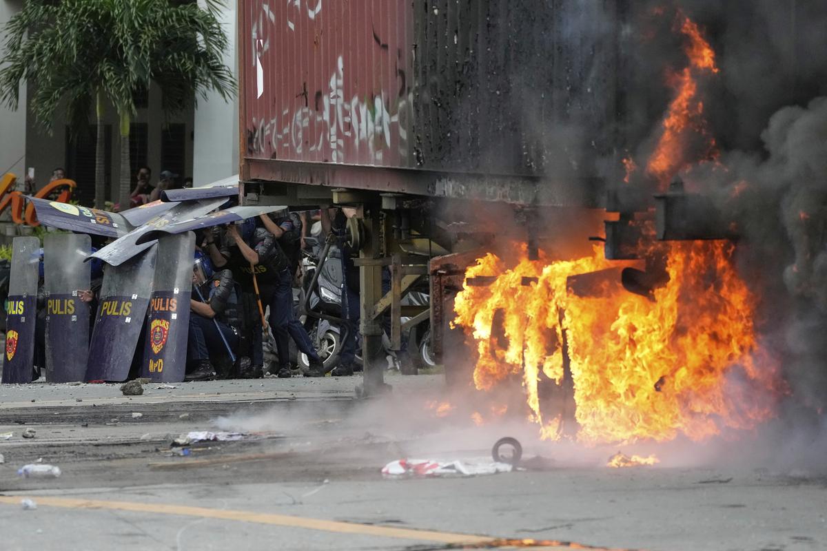 Police shield themselves beside a burning container during clashes with anti-corruption protesters in Manila, Philippines, Sunday, September 21, 2025.