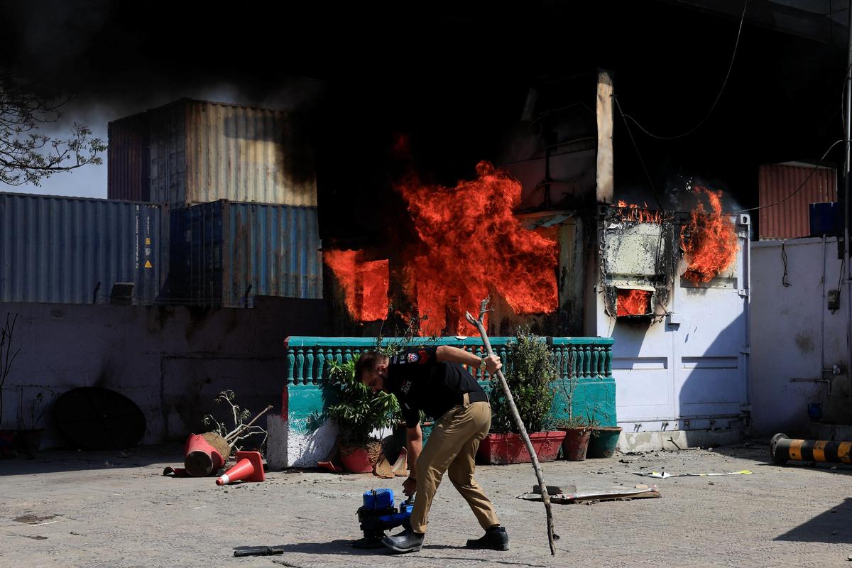 A police officer retrives items in front of a police checkpost burned by protesters near the U.S. Consulate General, following news of U.S. and Israeli strikes on Iran that killed supreme leader Ayatollah Ali Khamenei, in Karachi, on Mach 1, 2026