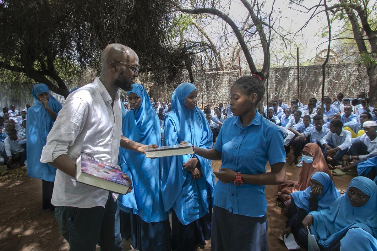 This handout picture taken on October 25, 2023 and made available on November 28, 2023 by the UNHCR shows Abdullahi Mire (left) distributing books to refugee students in Kenya’s Dadaab refugee camp. 