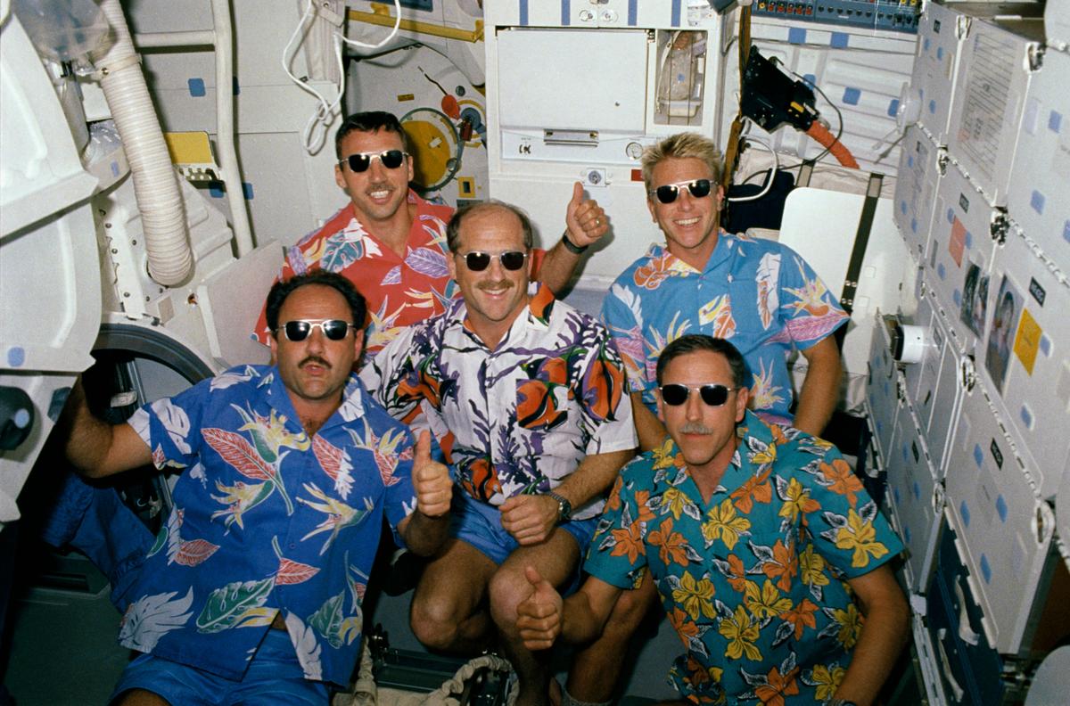 STS-26 crewmembers wear Hawaiian attire and sunglasses while giving the “thumbs up” signal as they pay tribute to the Hawaii tracking station during an unscheduled television downlink on October 2, 1988. 