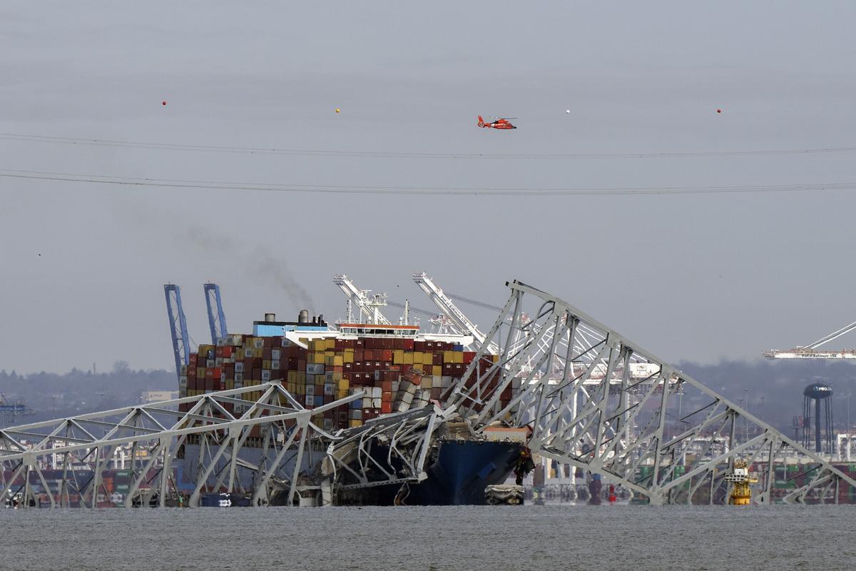 A helicopter flies over a container ship as it rests against wreckage of the Francis Scott Key Bridge on Tuesday, March 26, 2024, as seen from Pasadena, Md. 