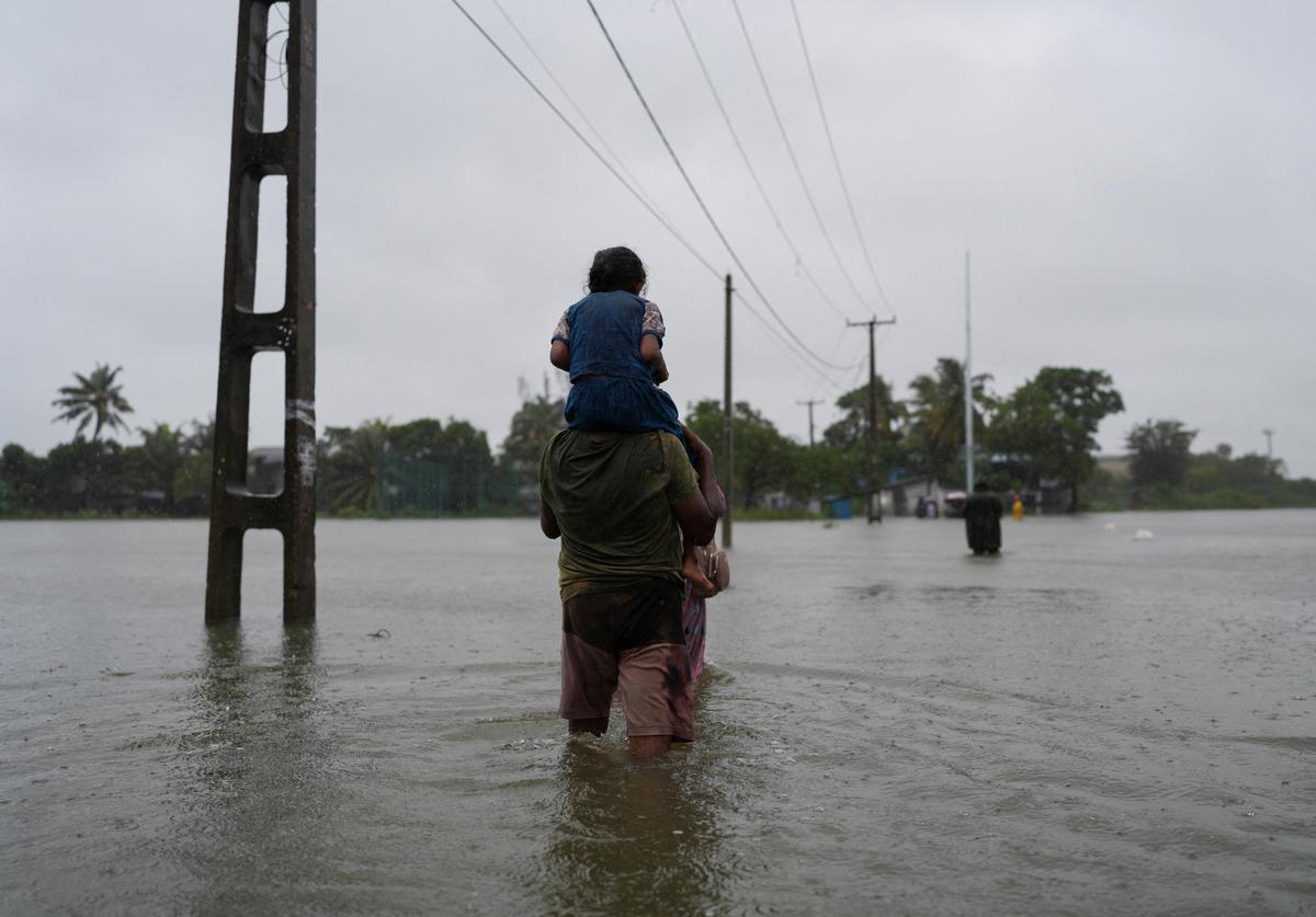 Um homem carregando uma criança no ombro atravessa uma rua inundada, após fortes chuvas em Wellampitiya, Sri Lanka, em 28 de novembro de 2025.