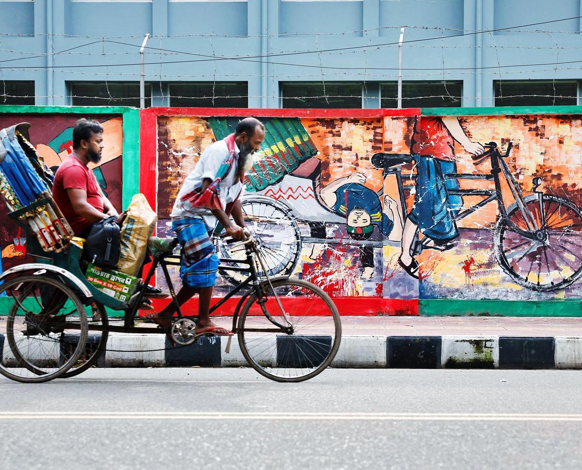 A rickshaw passes by graffiti depicting a rickshaw carrying a student's body during a protest at the University of Dhaka area in Dhaka, Bangladesh, September 3, 2024. A rickshaw passes by graffiti depicting a rickshaw carrying a student's body during a protest at the University of Dhaka area in Dhaka, Bangladesh, September 3, 2024.