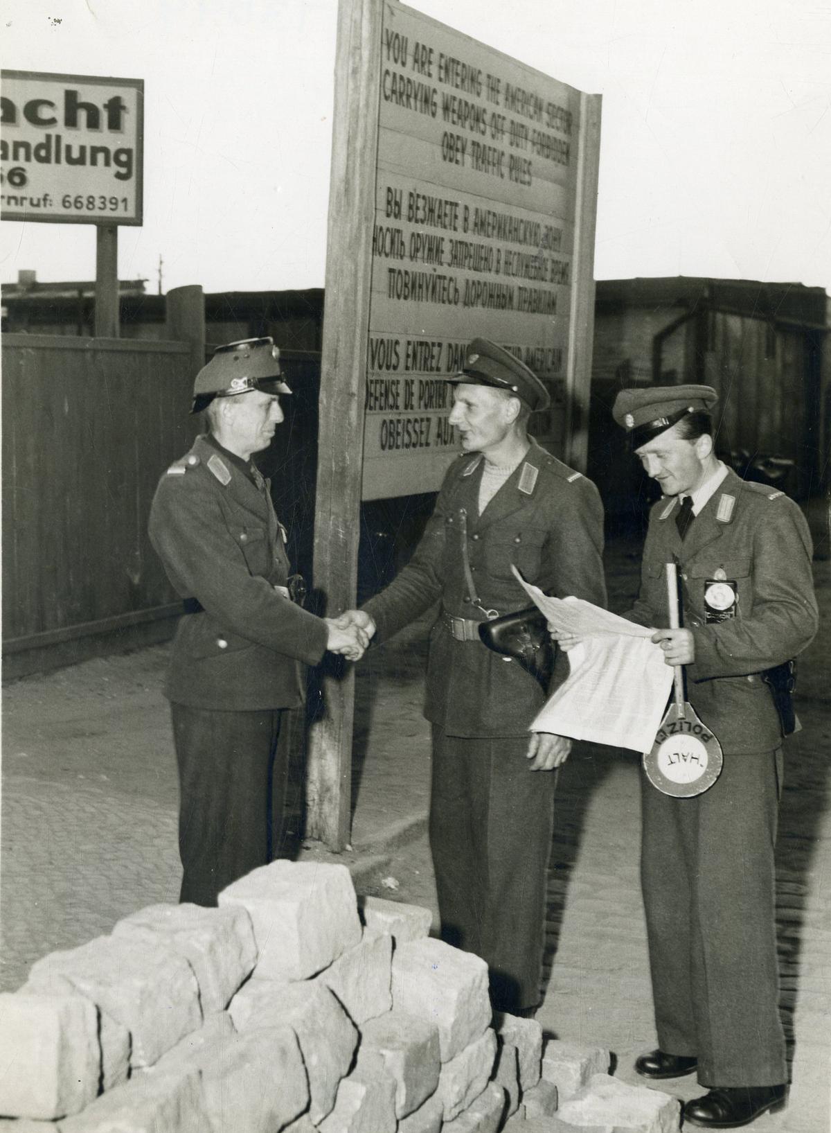 Hands on the border: News that the eleven-month-long Berlin blockade is to be lifted on May 12, 1949, leads to a handshake between a German policeman from the Eastern Sector (left) and his counterpart from the Western Sector at the Soviet-American Sector border in Berlin. A third policeman happily flips through a newspaper. PHOTO: THE HINDU ARCHIVES