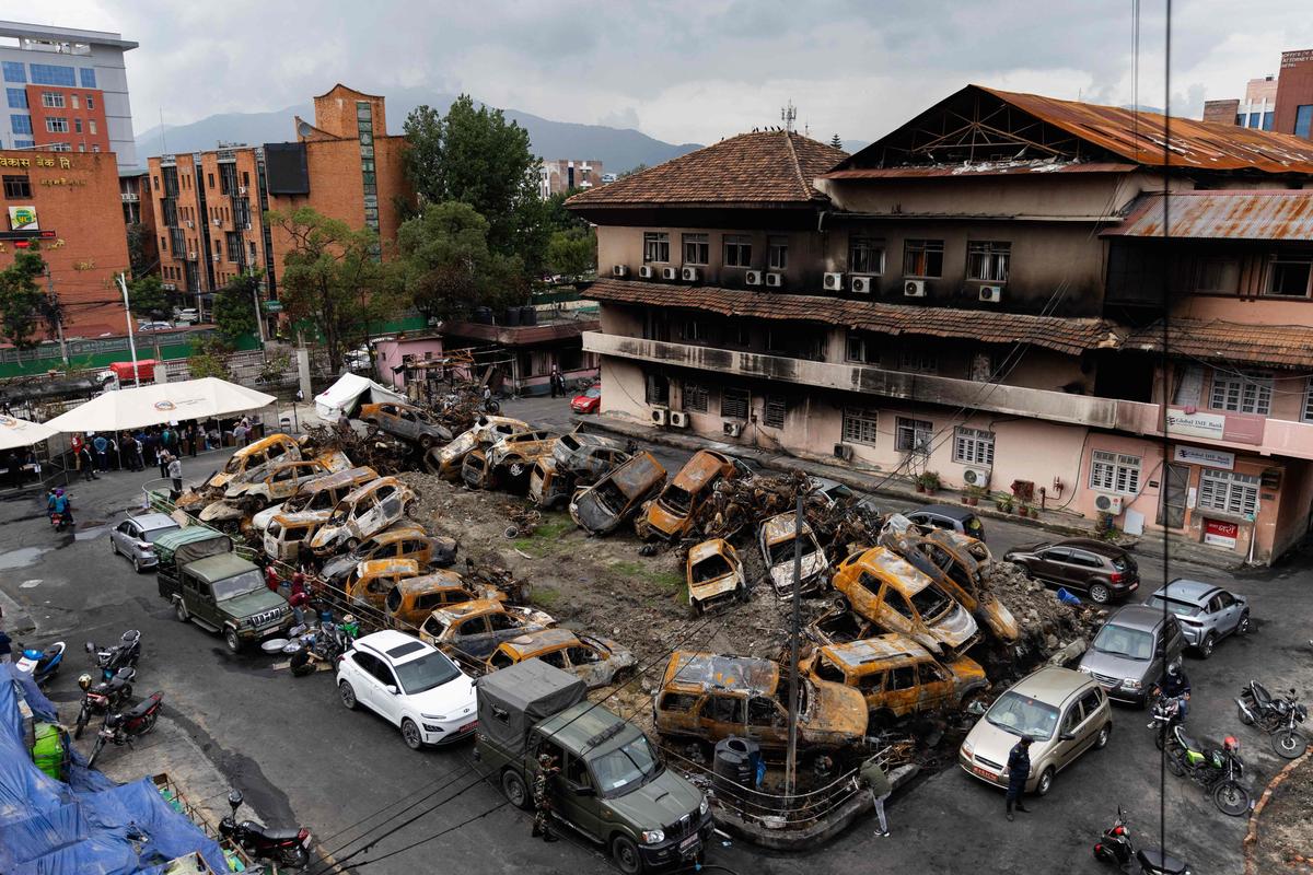 Court personnel gather under makeshift tents beside heaps of charred vehicles at the torched Supreme Court premises in Kathmandu on September 14, 2025, to provide legal services to Nepali nationals after judicial operations resumed. Nepal’s new leader Sushila Karki vowed on September 14, to follow protesters’ demands to “end corruption” as she began work as interim prime minister, after “Gen Z” youth demonstrations ousted her predecessor. 