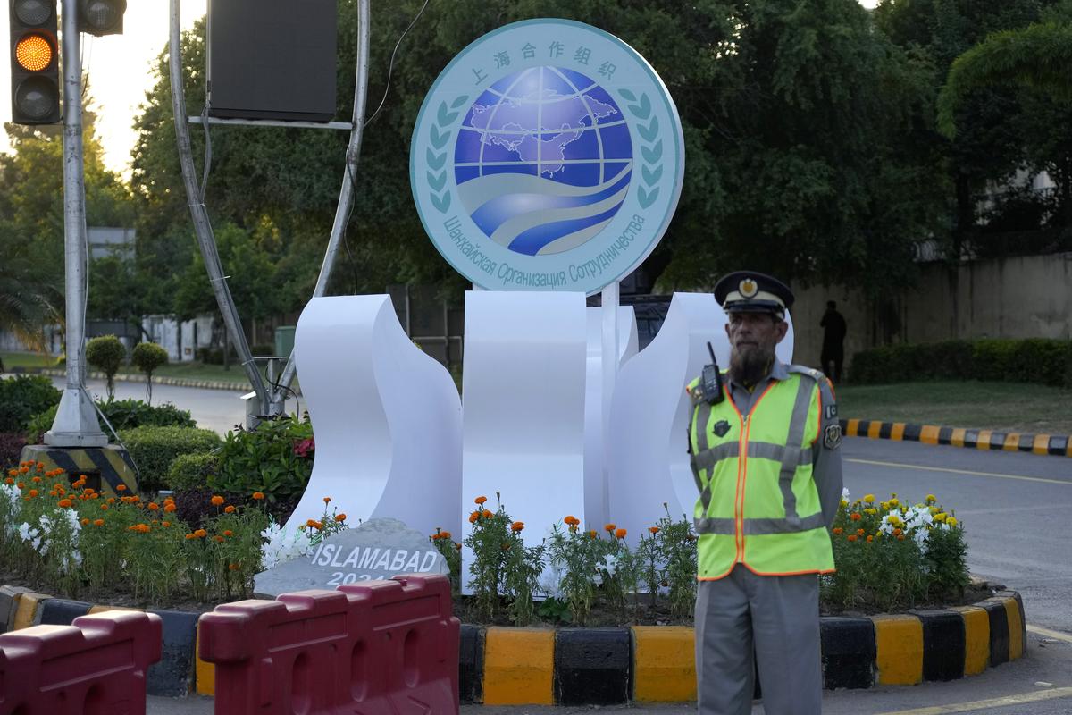 A traffic police officer stands next to the logo of the Shanghai Cooperation Organization (SCO) displayed on the road leading to the venue of the upcoming SCO summit in Islamabad.