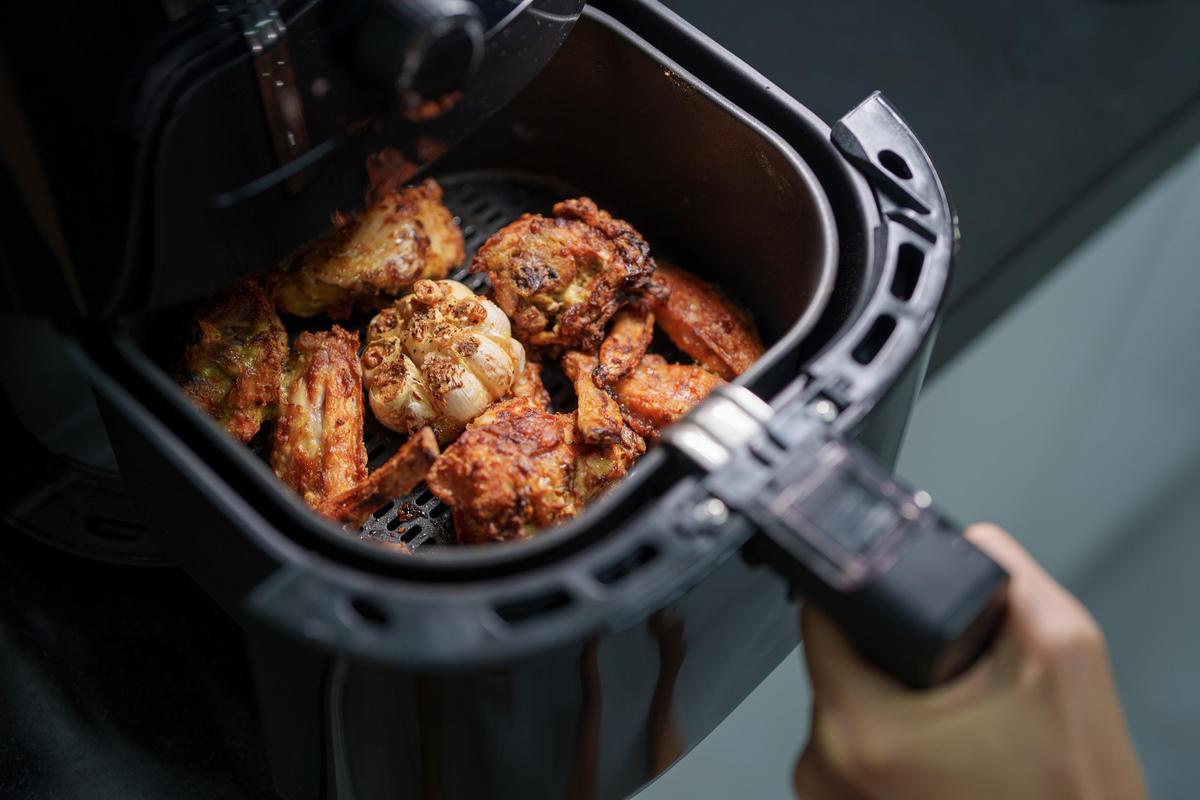 A woman is using an air fryer to prepare grilled chicken in her kitchen, focusing on a healthier cooking method with minimal oil. A woman is using an air fryer to prepare grilled chicken in her kitchen, focusing on a healthier cooking method with minimal oil.