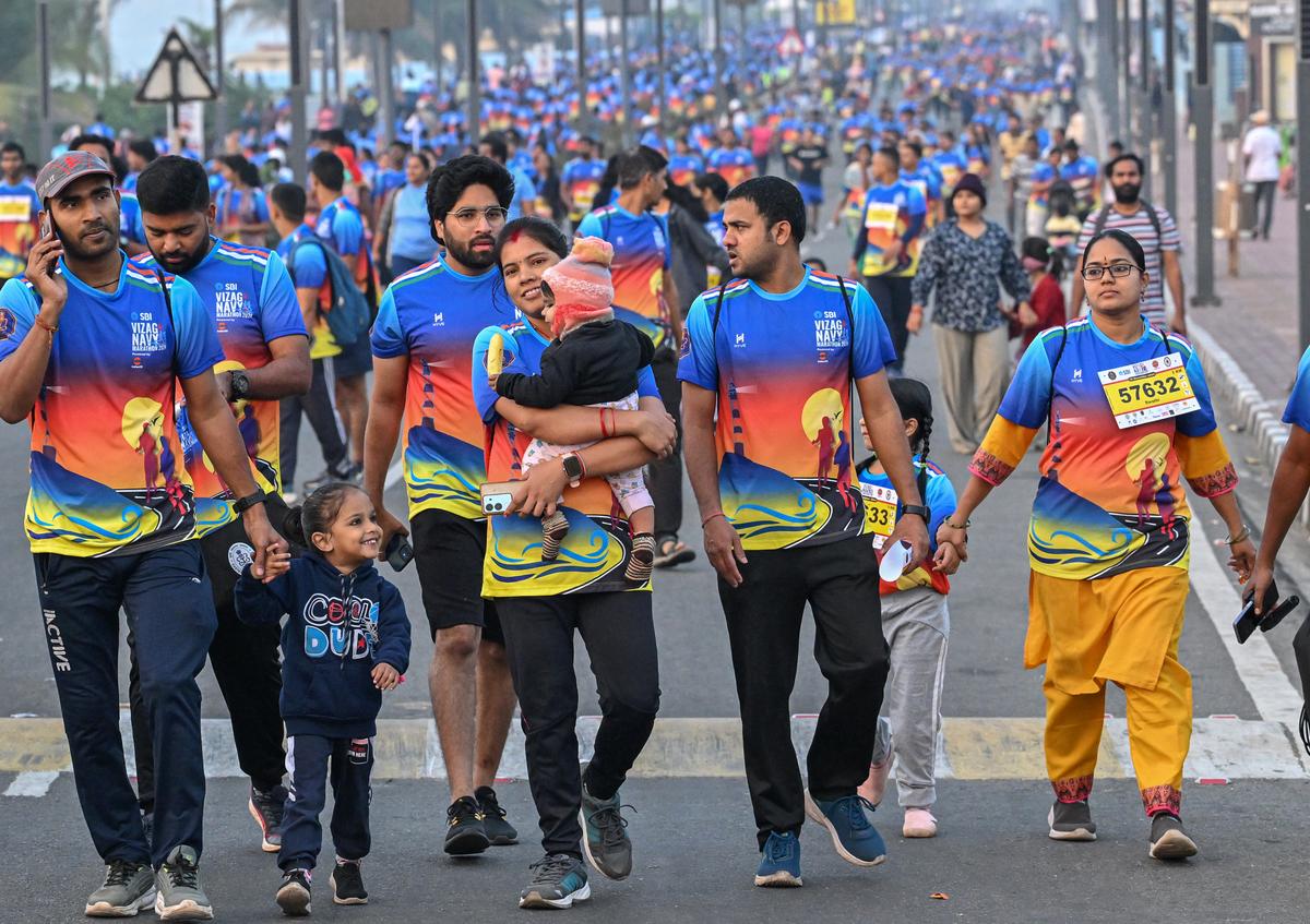 Parents carrying their children as people from all age groups participate in the Vizag Navy Marathon 2024, organised by the Indian Navy at the Beach Road in Visakhapatnam on Sunday.