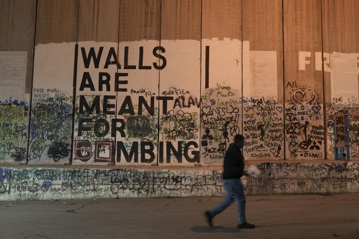 A man walks past a barrier with a mural that reads ‘Walls are meant for bombing’, in the West Bank city of Bethlehem.