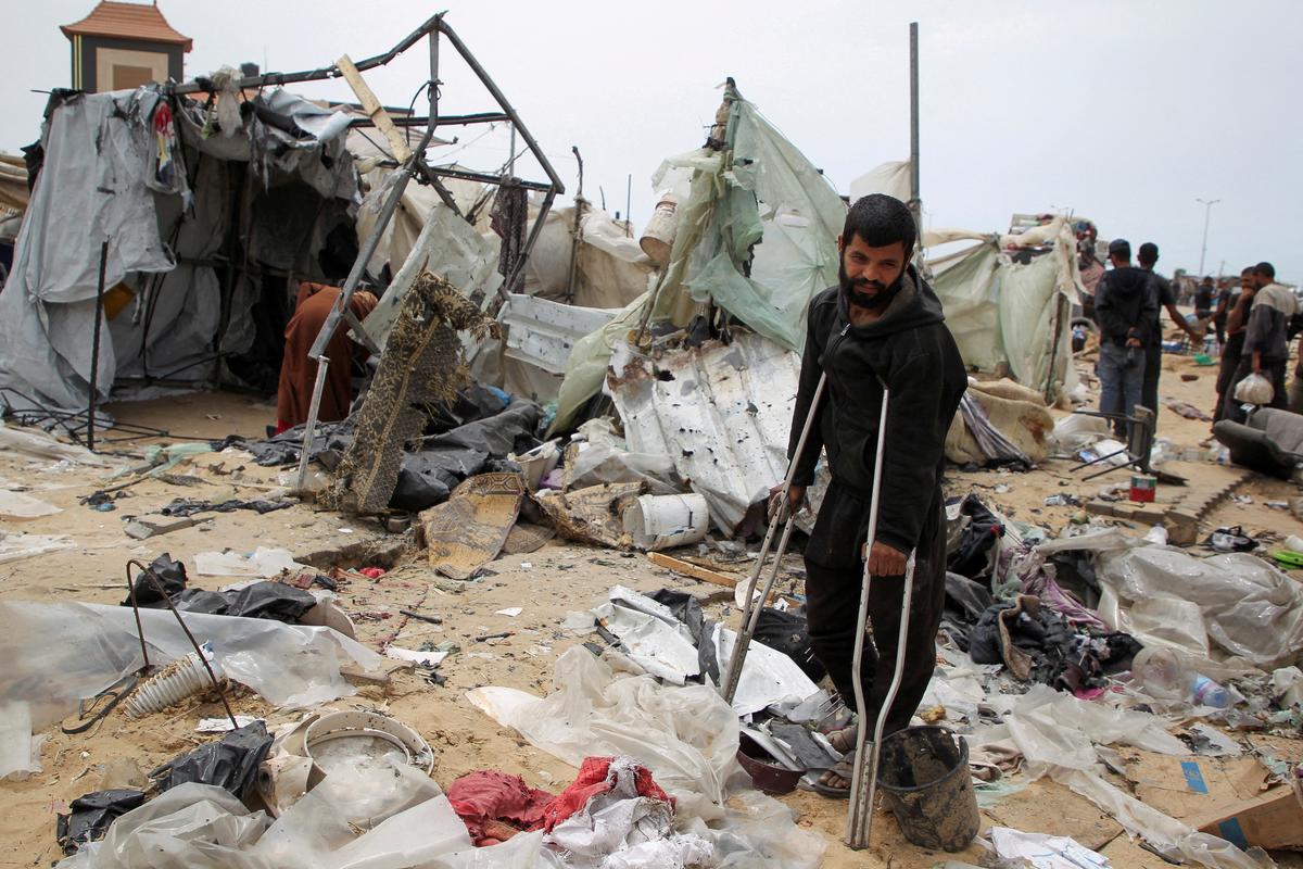 A man looks on as Palestinians inspect a tent camp damaged in an Israeli strike during an Israeli military operation, in Rafah, in the southern Gaza Strip, on May 28, 2024.