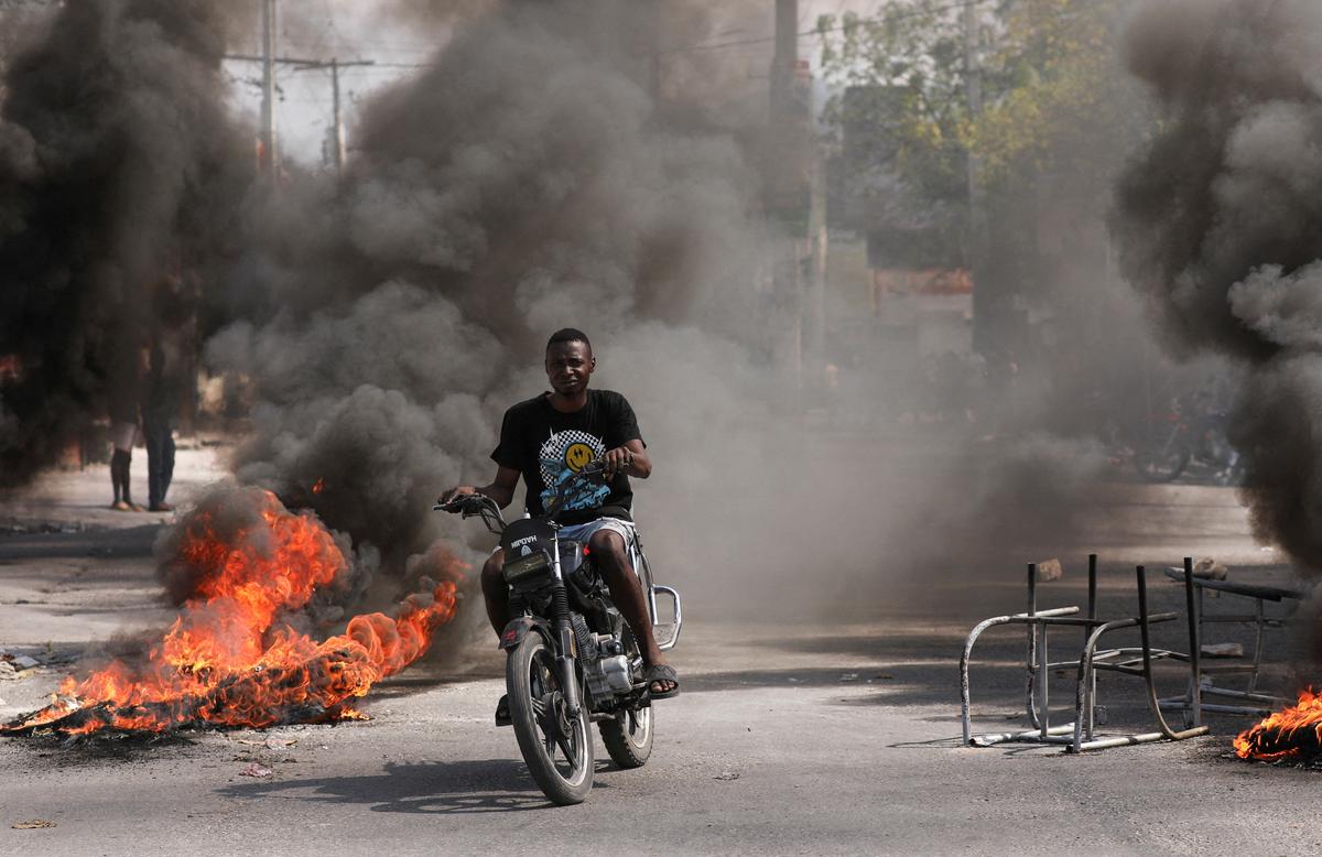 A man drives past a burning barricade during a protest against Prime Minister Ariel Henry’s government and insecurity, in Port-au-Prince, Haiti March 1, 2024.