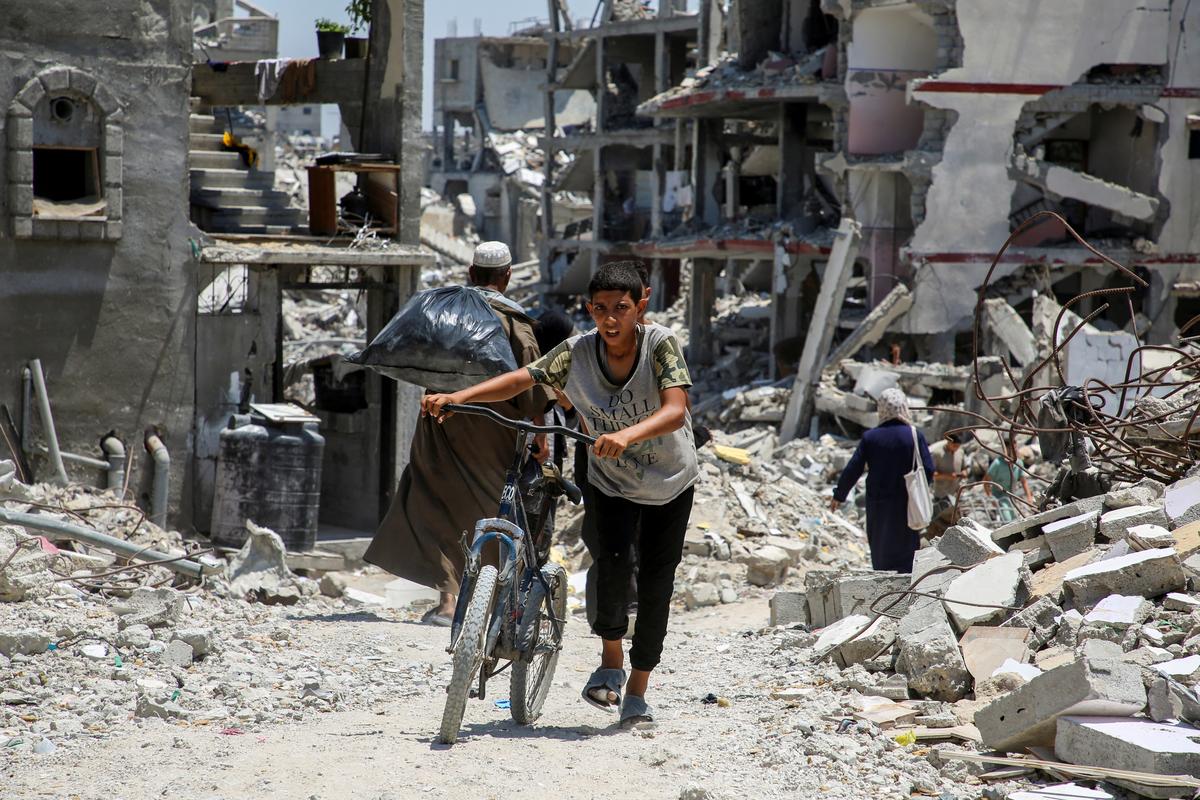 A Palestinian pushes a bicycle as he walks past the rubble of houses destroyed during the Israeli military offensive, amid the Israel-Hamas conflict, in Khan Younis in the southern Gaza Strip on July 10, 2024. 