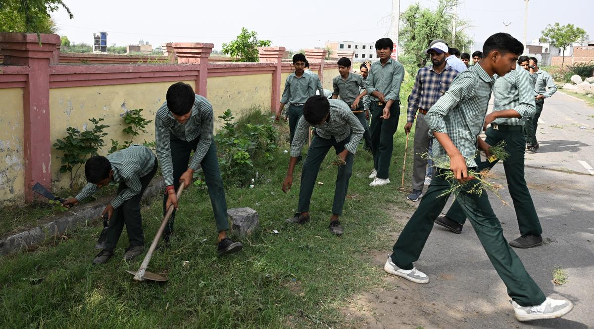 Students cut and clear the grass near the boundary wall of a government school in Nuh. Students cut and clear the grass near the boundary wall of a government school in Nuh.