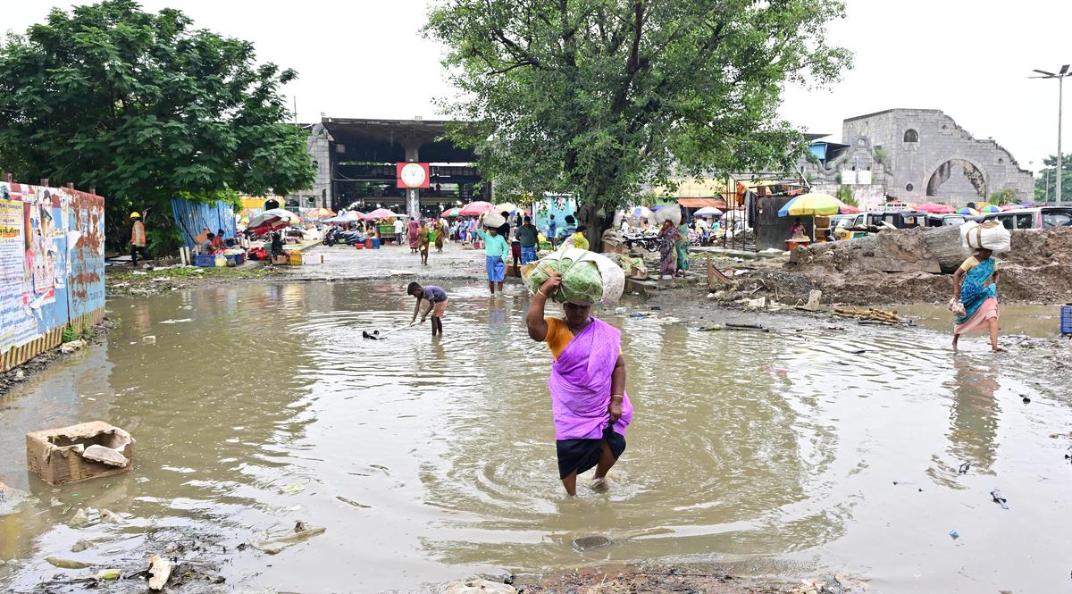 People wade through stagnant rainwater at the Koyambedu flower market in Chennai on October 24, 2025. 
