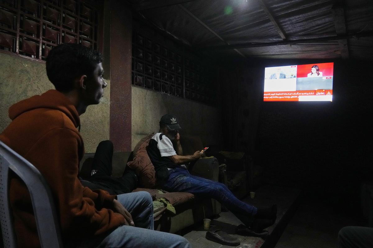 Palestinians follow the news on a television after the announcement that Israel and Hamas have agreed to the first phase of a peace plan to pause fighting, as they sit in a tent outside Al-Aqsa Hospital, in Deir al-Balah, in the central Gaza Strip, on Thursday, Oct. 9, 2025. 