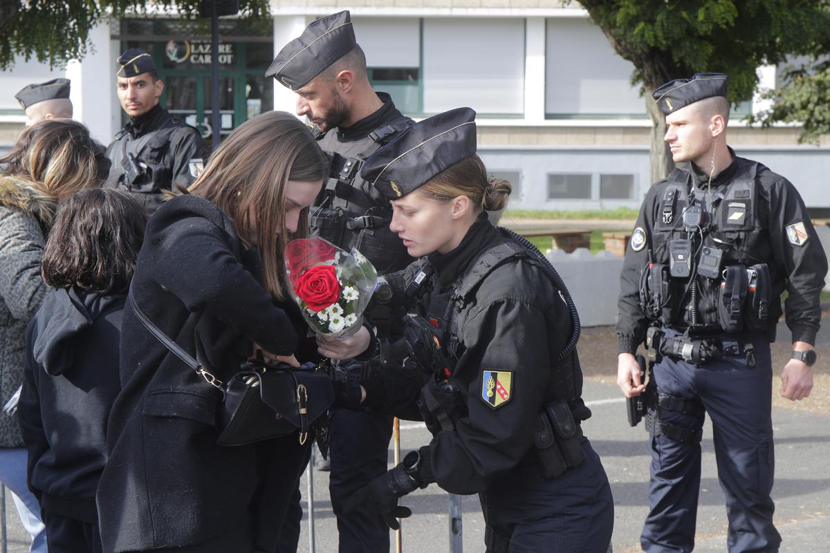 A police officer checks a handbag from a woman carrying flowers at the entrance of the Gambetta high school, Monday, Oct. 16, 2023 in Arras, northern France.  