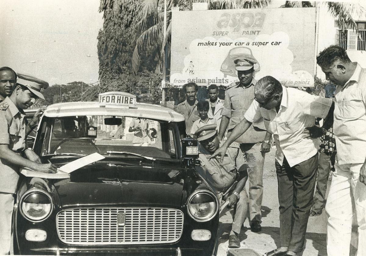 हम पृष्ठभूमि में होर्डिंग की पुष्टि नहीं कर सकते, लेकिन टैक्सीमीटर ने कैब को सुपर बना दिया है। यह आपके लिए आश्चर्य की बात हो सकती है, लेकिन एक समय था जब मोटर वाहन निरीक्षक टैक्सी किराया मीटर की सील की जांच करते थे। ये तस्वीर चेन्नई में हुई ऐसी ही एक औचक छापेमारी की है.