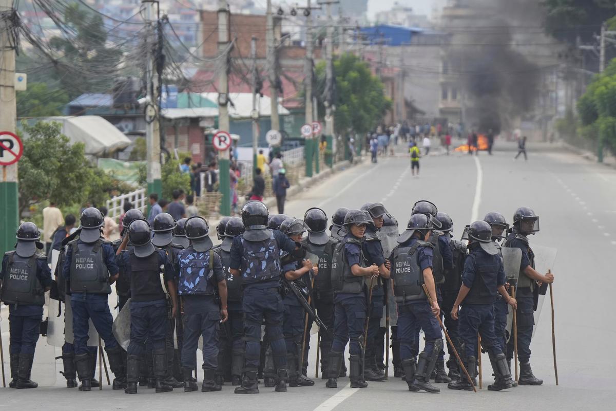Policemen in riot gear stand guard on a street as protesters burn tires violating curfew orders in Kathmandu, Nepal, on September 9, 2025.