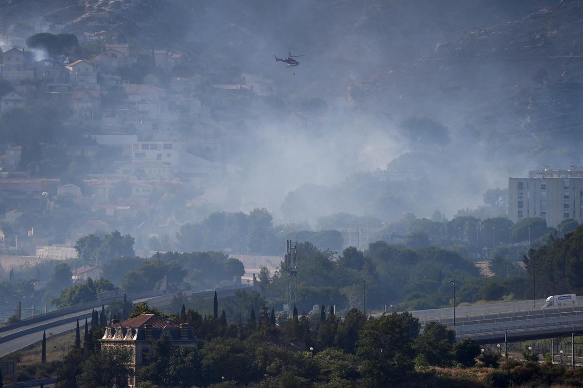 A helicopter flies over smoke rising from a fast-moving wildfire spreading on the outskirts of Marseille, southern France, July 8, 2025. 