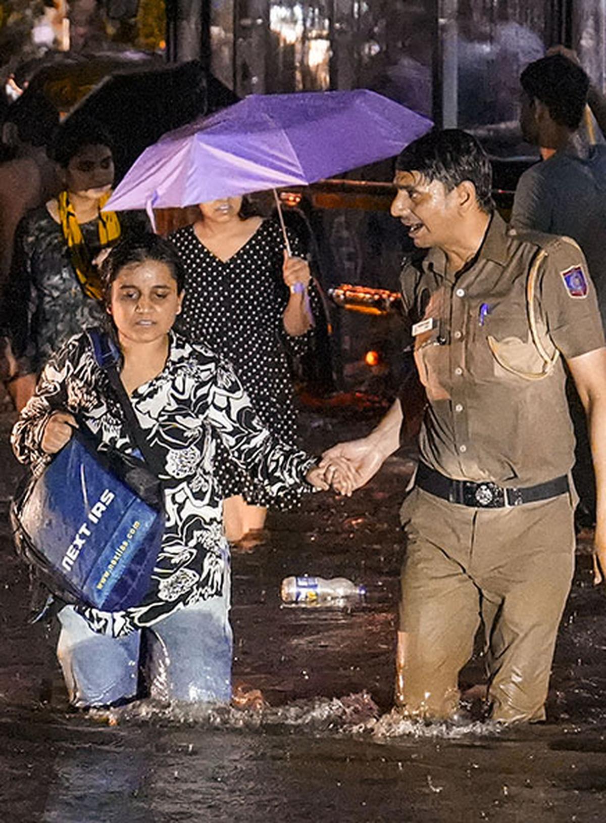 A woman being assisted by a police official while wading through a waterlogged road during rain near Old Rajinder Nagar area, in New Delhi. | Photo Credit: PTI