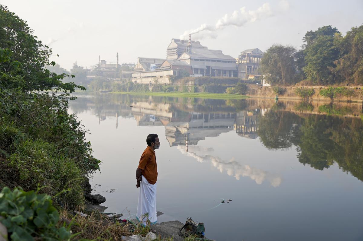 Adam Kutty stands on the bank of the Periyar River with smokestacks in the distance in Eloor, Kerala state, India, Friday, March 3, 2023. Many of the petrochemical nearby produce pesticides, rare earth elements, rubber processing chemicals, fertilizers, zinc-chrome products and leather treatments. 