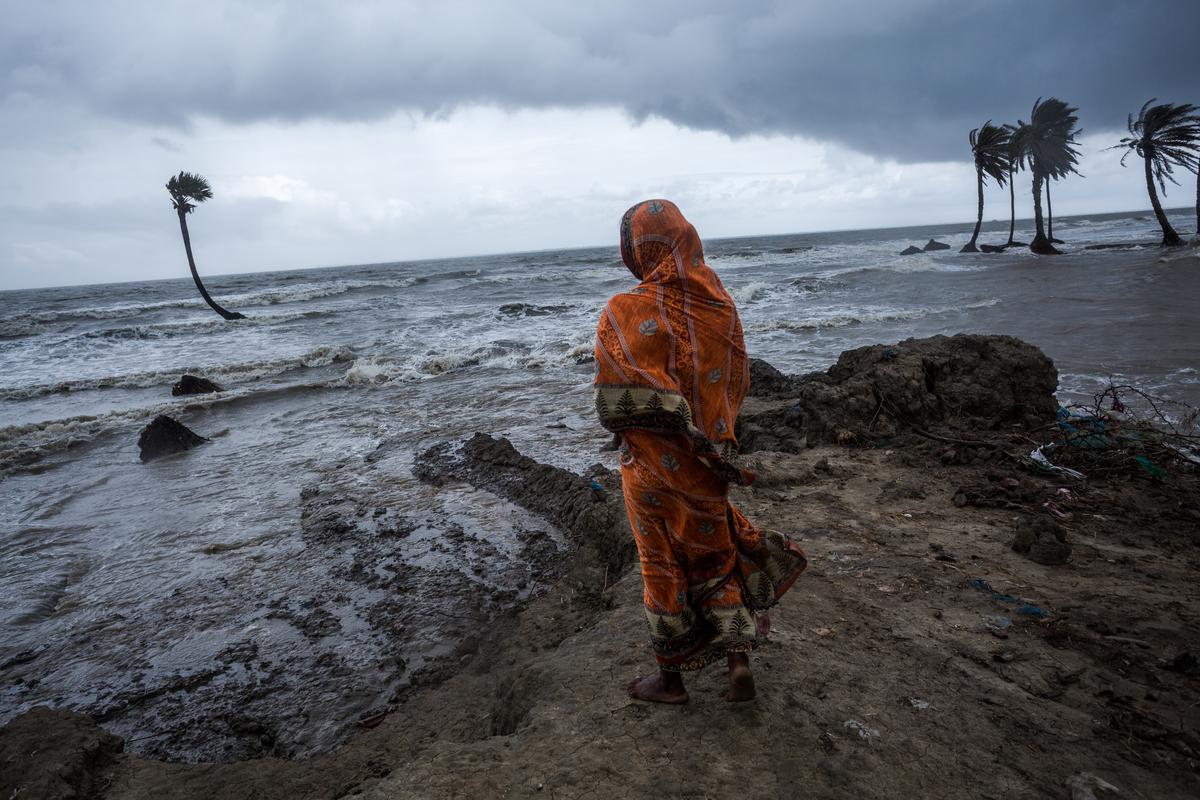 A woman stands in front of her house submerged in water due to tidal flooding in the Sundarbans