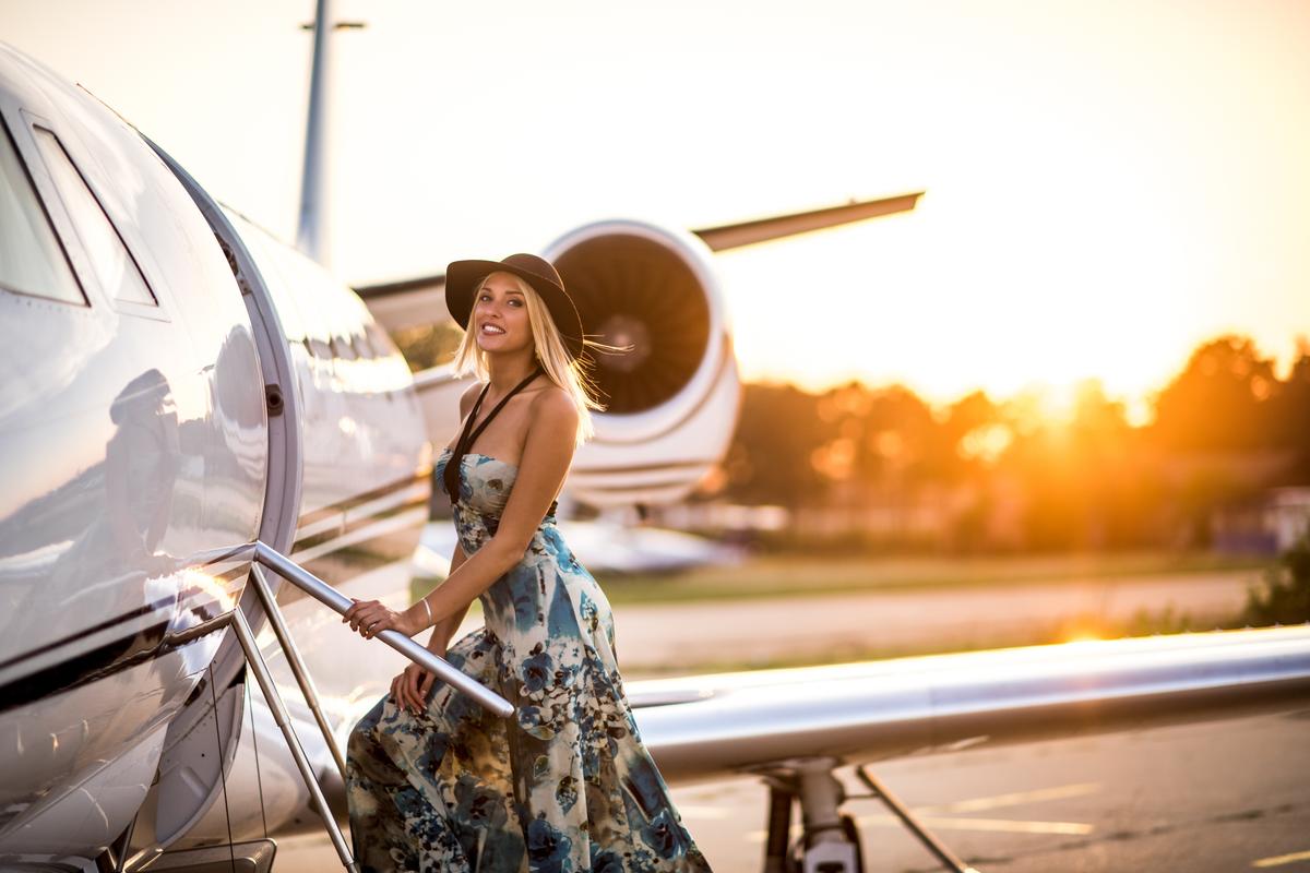 Young woman standing on the stairs of private jet airplane.