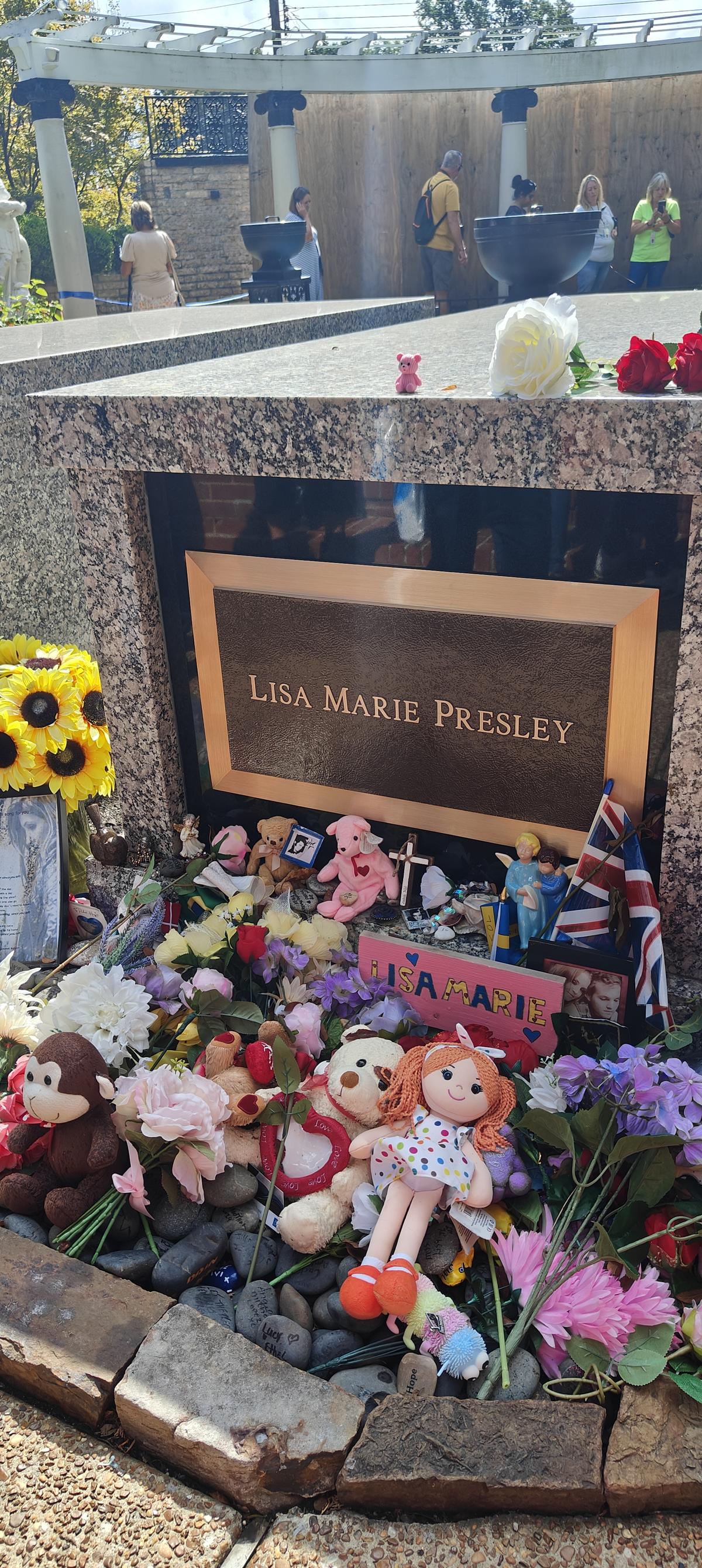 Lisa Marie Presley’s grave is piled with teddy bears, dolls, and flowers.  