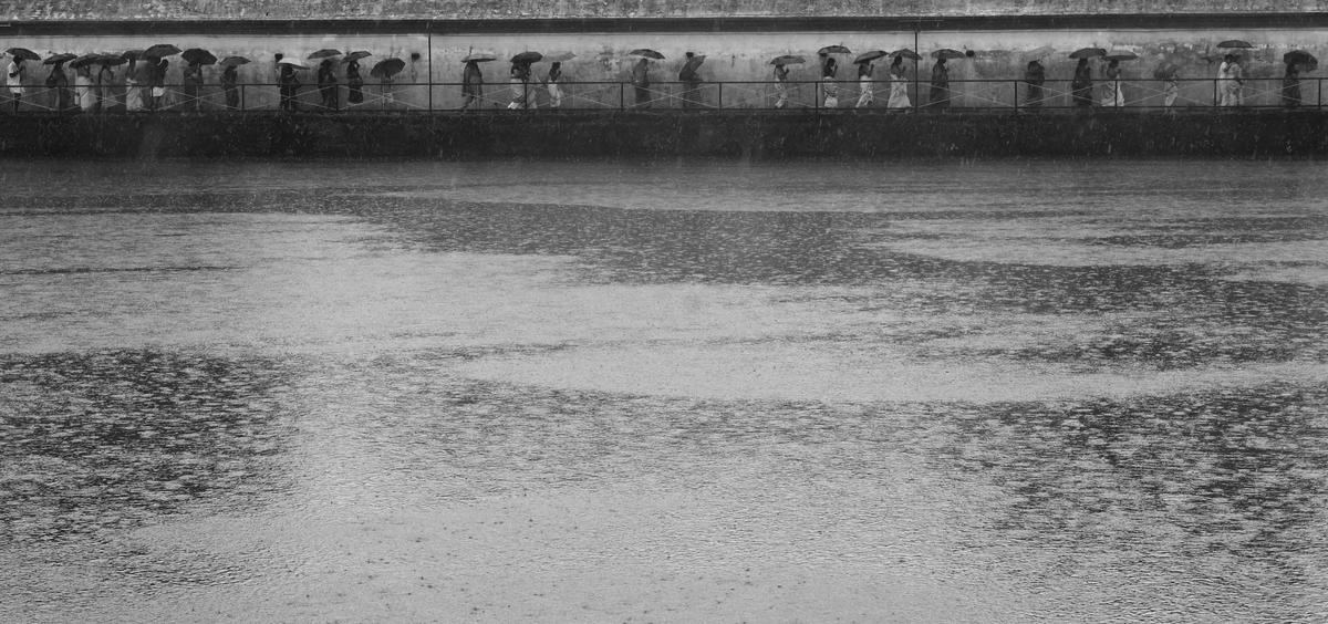 Devotees circumambulate the temple pond in heavy rain at Koodalmanikyam Temple, Irinjalakuda 