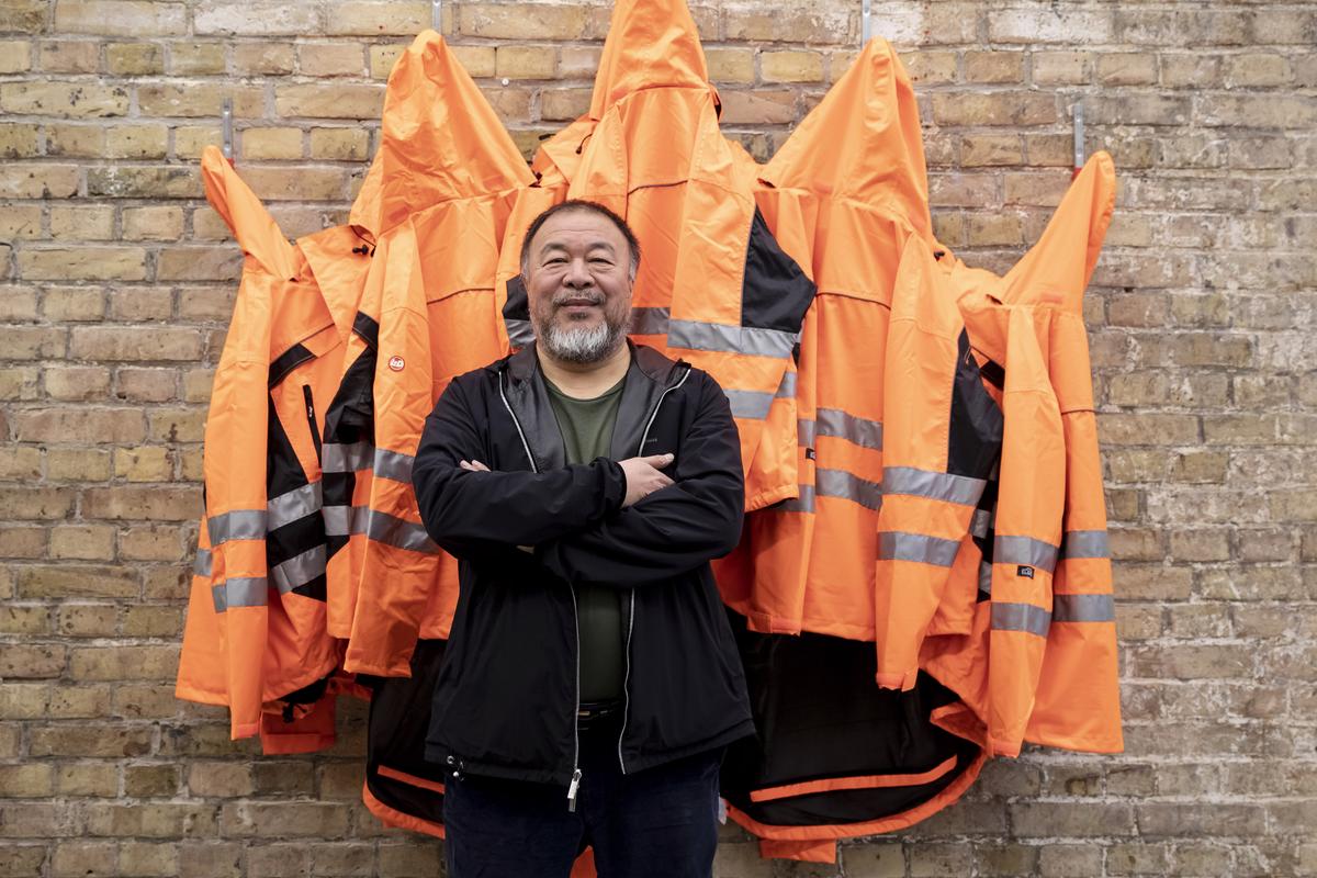 Ai Weiwei standing in front of his artwork Safety Jackets Zipped the Other Way