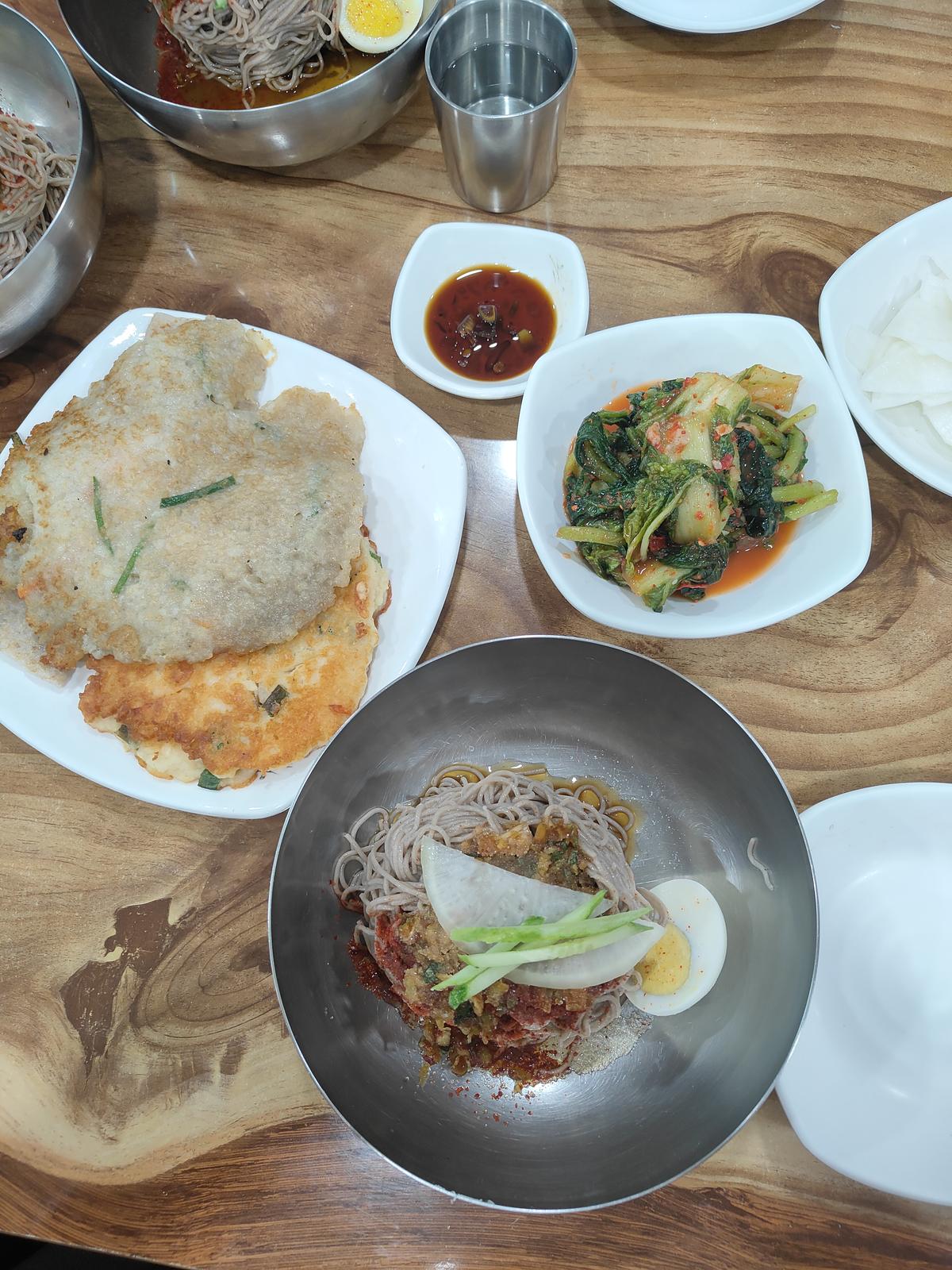A bowl of makguksu with banchan(side dishes) and jeon (pancakes)