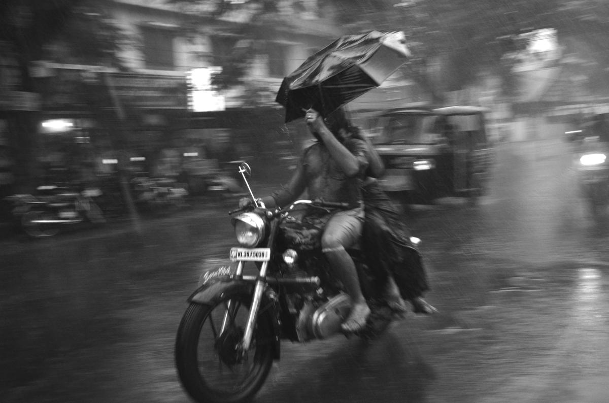 A bike rider tries to shield himself with an umbrella in Kochi