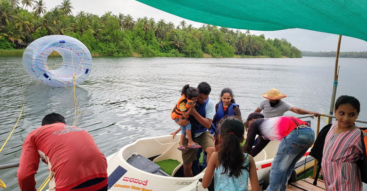 A family lands on the makeshift jetty after completing a speed boat ride in Souparnika River arranged by Maravanthe Adventure Sports on May 21, in Maravanthe, Byndoor Taluk, Udupi district. A zorbing cylinder is seen in the background.