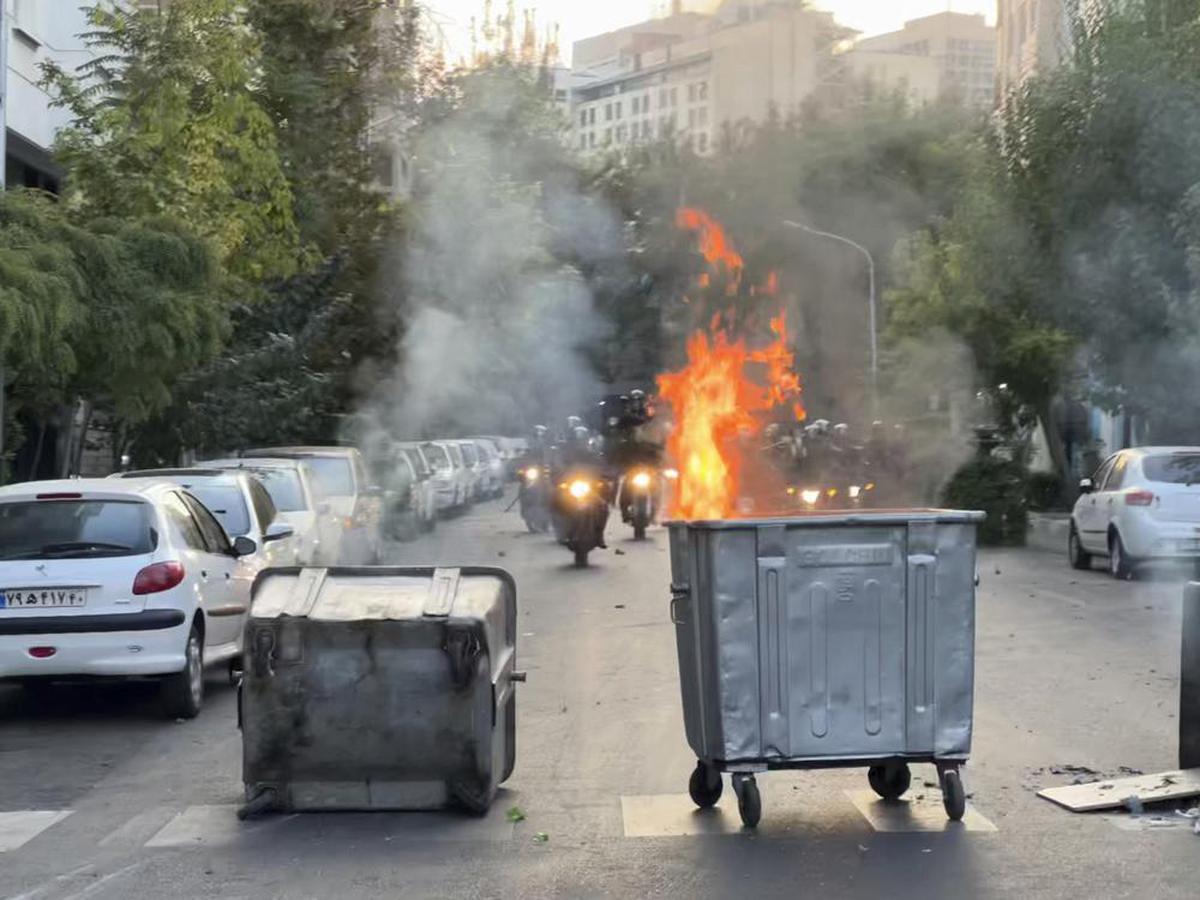 A trash bin is burning as anti-riot police arrive during a protest in Tehran on September 20, 2022.