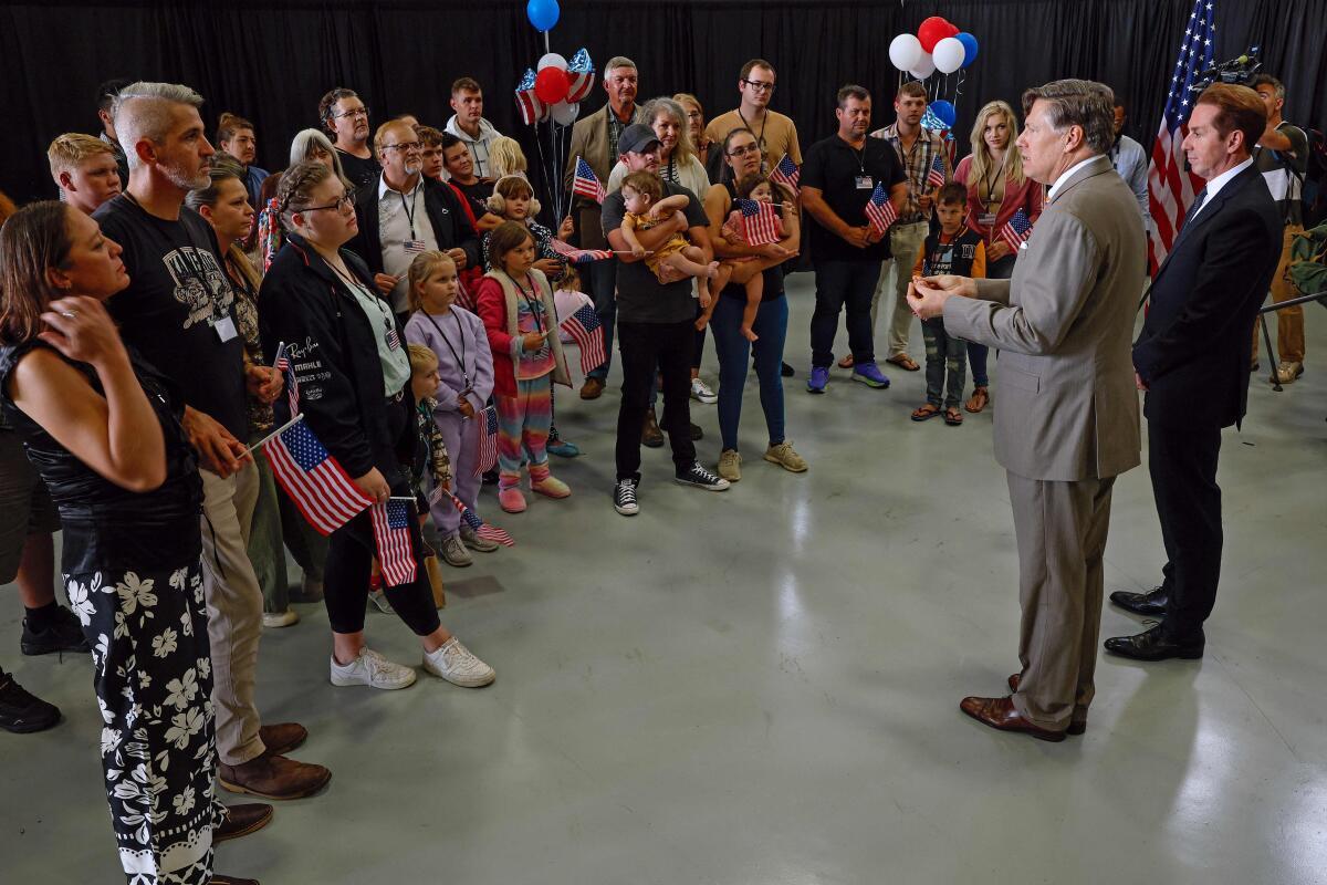 Newly arrived South Africans listen to U.S. Deputy Secretary of State Christopher Landau and Homeland Security Deputy Secretary Troy Edgar (R) deliver welcome statements in a hangar at Atlantic Aviation Dulles near Washington Dulles International Airport on May 12, 2025 in Dulles, Virginia. 