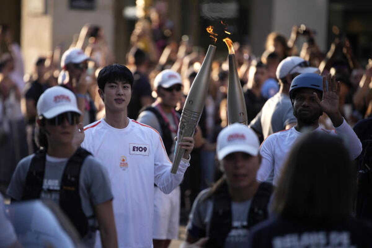 Jin, left, the oldest member of K-pop supergroup BTS, takes the Olympic torch, Sunday, July 14, 2024 in Paris. Jin will carry the Olympic torch in the area of Paris’ Louvre Museum after recently completing his mandatory military service. 