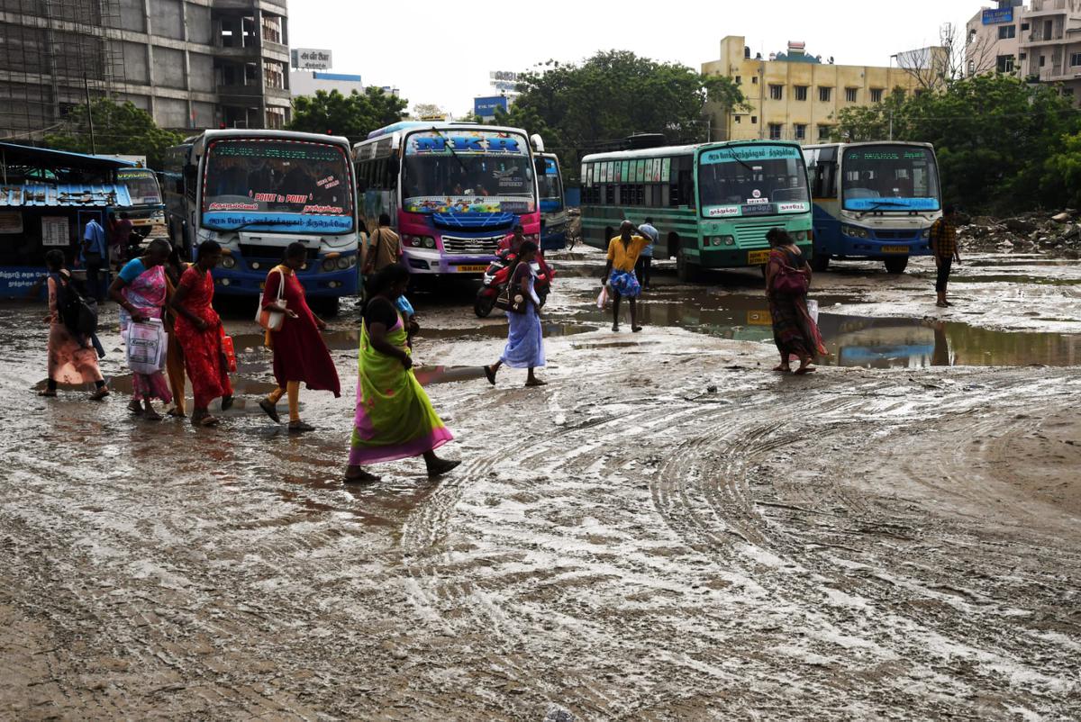 Passengers walk through stagnated rain water at the temporary bus stand in Thoothukudi on November 2, 2022