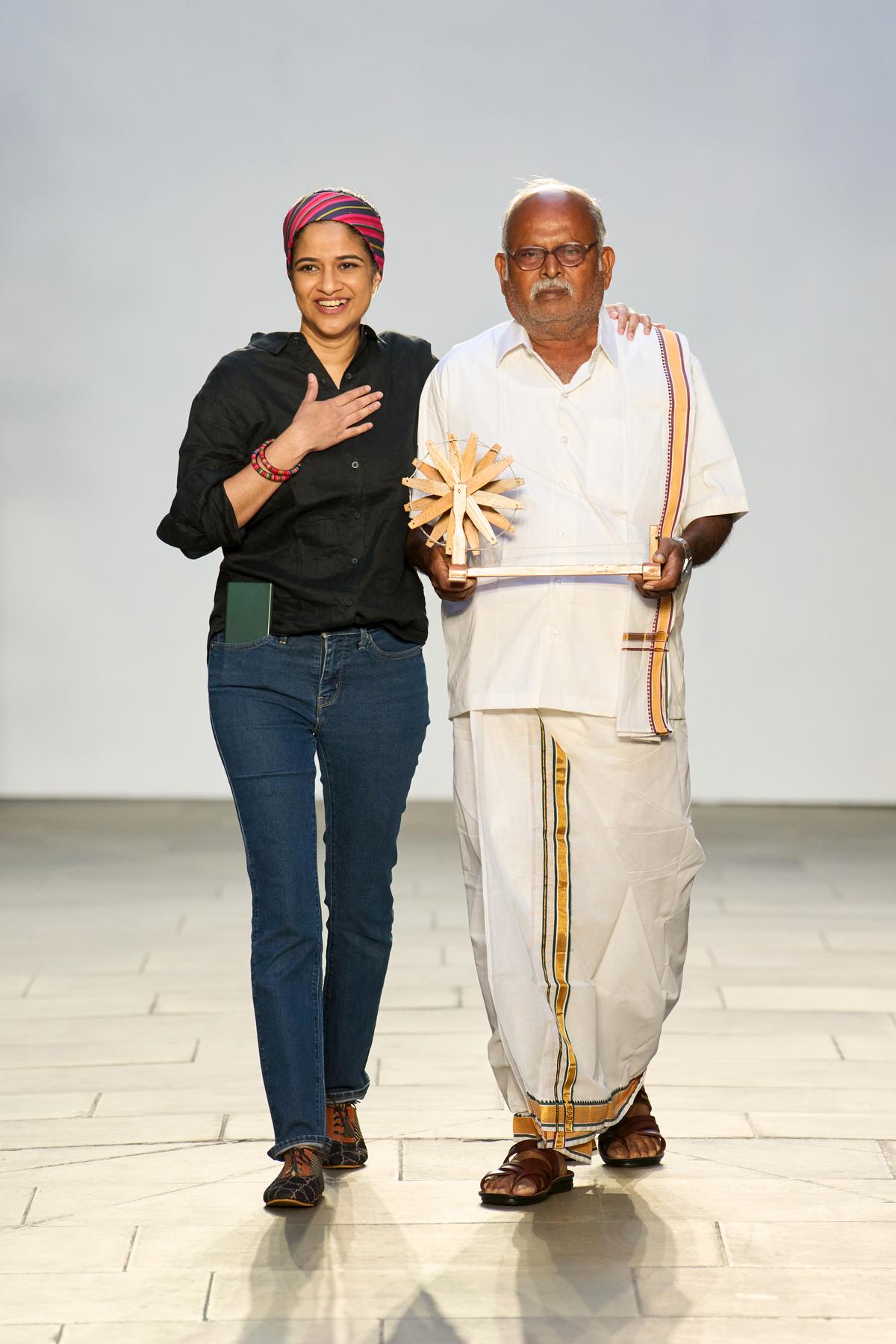 Dubai-based designer Vino Supraja walks the ramp with Mr. Sakthivel, who carries a model of a spinning wheel (raattai) Dubai-based designer Vino Supraja walks the ramp with Mr. Sakthivel, who carries a model of a spinning wheel (raattai)