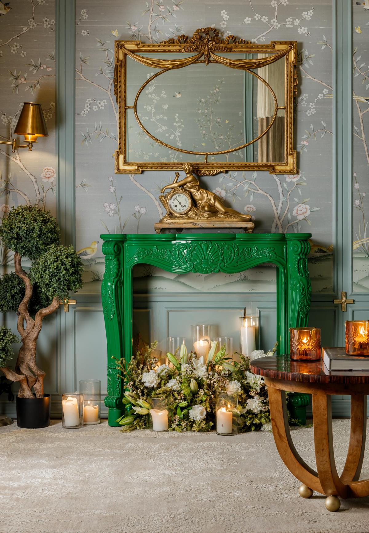Elegant green fireplace adorned with candles and floral arrangements against a floral wallpaper. Elegant green fireplace adorned with candles and floral arrangements against a floral wallpaper.