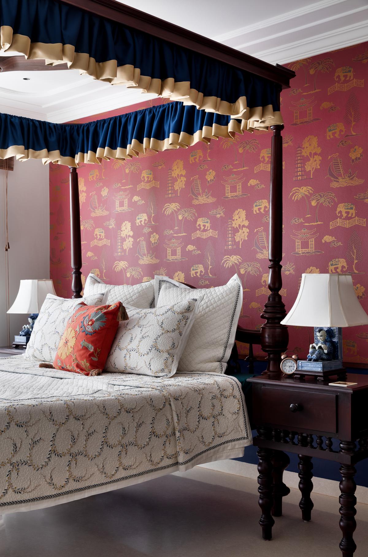 Traditional florals and Mughal-inspired motifs play out on a vibrant red wall, framing the stately four-poster bed. Traditional florals and Mughal-inspired motifs play out on a vibrant red wall, framing the stately four-poster bed.